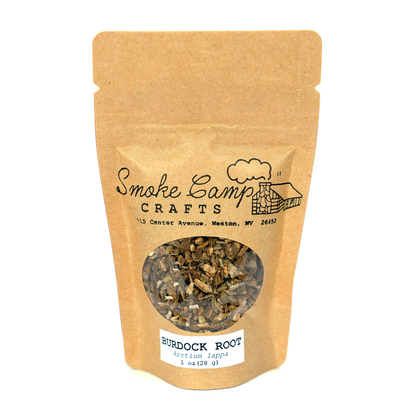 A brown paper pouch of Smoke Camp Crafts Burdock Root, Dried, 1oz features a window displaying the root pieces and a white label with “BURDOCK ROOT, Arctium lappa, 1 oz (28 g)”; brand name and address are on the package.