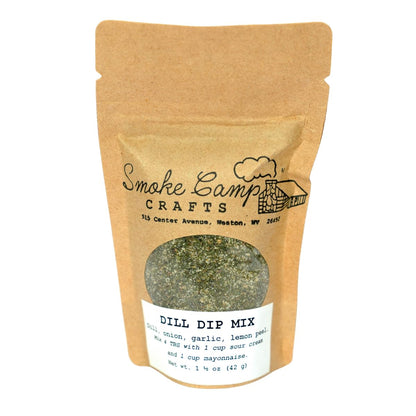 A brown paper pouch labeled “Smoke Camp Crafts Herbal Seasoning Blend - Dill Dip Mix, 1.5 oz” shows green herb mix through a clear window. The label highlights ingredients, serving ideas, and the trusted Smoke Camp Crafts brand.